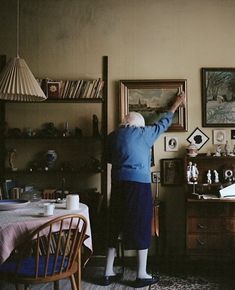 an older woman standing in front of a desk with a lamp on top of it