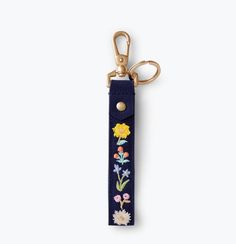 a keychain with embroidered flowers on the front and back, hanging from a gold metal hook