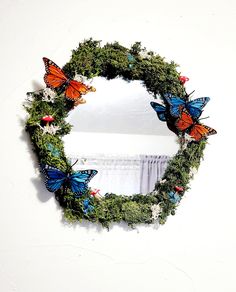 a wreath with butterflies on it hanging from the wall next to a mirror that is decorated with greenery