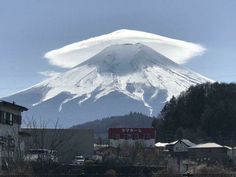 a large white cloud is in the sky over a mountain with houses and trees around it