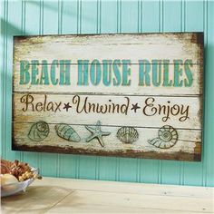 a wooden sign that says beach house rules relax unwind enjoy on the wall next to a bowl of seashells