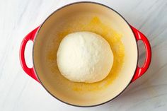 a ball of bread in a red pot on a white counter top with yellow liquid