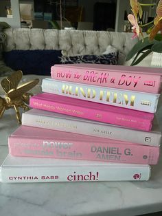 a stack of pink books sitting on top of a table next to a vase with flowers