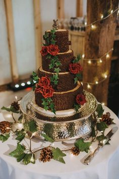 a three tiered cake decorated with red roses and greenery sits on a table