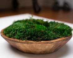 a wooden bowl filled with green moss on top of a table