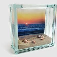 two seashells in the sand under an acrylic block with sunset on the horizon