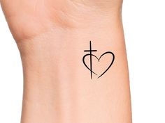 a cross and heart tattoo on the left side of the wrist, with an arrow in the center