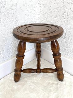 a small wooden stool sitting on top of a white carpeted floor next to a wall