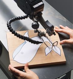 a person is using a camera to cut out a fish on a piece of wood