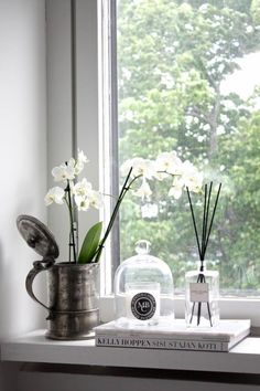 some white flowers are in a vase on a window sill next to a book