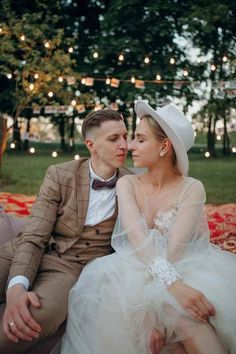 a man and woman are sitting on a bench in front of some trees with lights