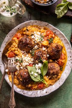 meatballs and pasta in a white bowl on a green table with utensils