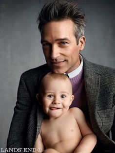 a man holding a baby in his lap and smiling at the camera while wearing a suit