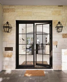 an open glass door with two hanging lights on the wall and a rug in front of it