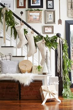 christmas stockings hanging from the banister in front of stairs decorated with greenery and other holiday decorations