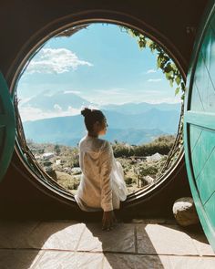 a woman sitting in front of a window looking out at the mountains and hills behind her