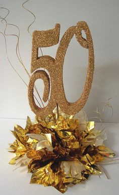 a gold 50th birthday cake topper on a white table with confetti and streamers