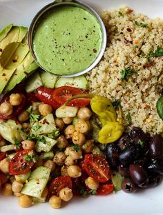 a white plate topped with rice, beans and veggies next to a bowl of sauce