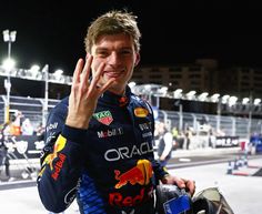 a man in a red bull racing suit waves to the crowd while holding his helmet