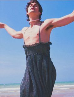 a man standing on top of a beach next to the ocean with his arms outstretched