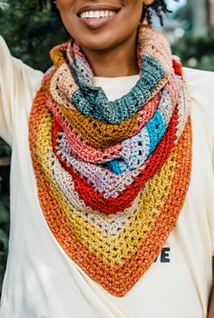 a smiling woman wearing a multicolored crocheted scarf on her neck and white t - shirt