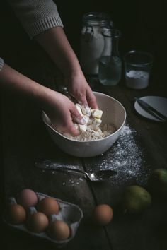 someone is mixing ingredients in a bowl on a wooden table with eggs and other kitchen utensils