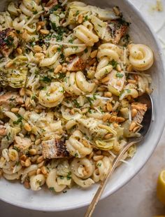 a white bowl filled with pasta and chicken on top of a table next to lemons