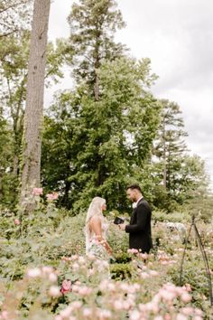 a bride and groom standing in the middle of a field with pink flowers on it