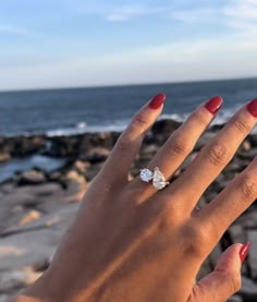 a woman's hand with a ring on top of her finger next to the ocean