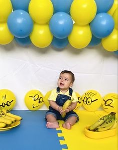 a baby sitting on the floor with bananas in front of him and balloons behind him