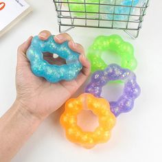 a hand holding a doughnut next to five different colored donuts in front of a wire basket