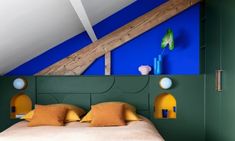 a bed in a room with green walls and yellow pillows on the headboard, next to a blue wall