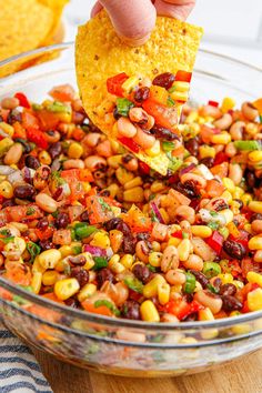 a person holding a tortilla chip over a bowl filled with beans and corn