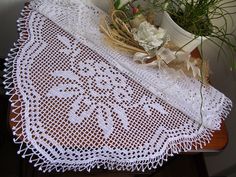 a white doily on a table with some flowers in the vase and two plants