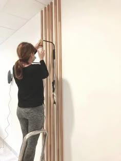 a woman standing on a stepladder in front of a wall with wood slats