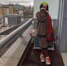 a woman with bright green hair is standing on a balcony holding a basketball and looking at the camera