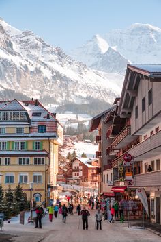 people are walking down the street in front of some buildings with mountains in the background