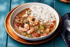 a white bowl filled with shrimp and rice on top of a wooden table next to a spoon