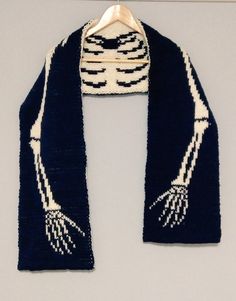 a knitted scarf with white and black designs on the edges, hanging from a hanger