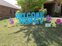 a welcome home sign in front of a house with balloons and stars on the lawn