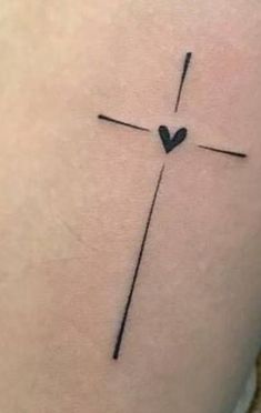 a cross tattoo on the back of a woman's thigh with a heart in it