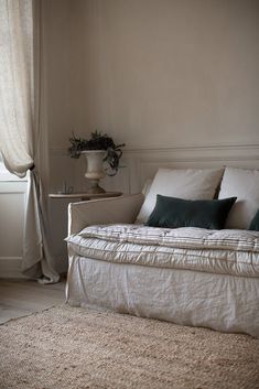 a white couch sitting in front of a window next to a table with a vase on it