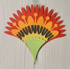 an orange and green paper flower hanging on a white wooden wall next to a string