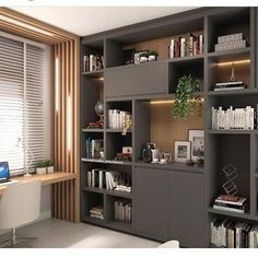 a computer desk sitting under a window next to a bookshelf filled with books