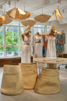 three mannequins wearing hats and dresses in a room with hanging lights above them