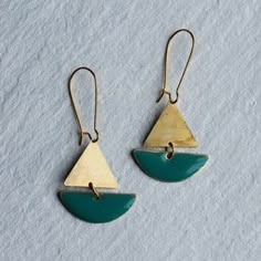 two green and gold earrings sitting on top of snow covered ground with one earring in the shape of an upside down triangle