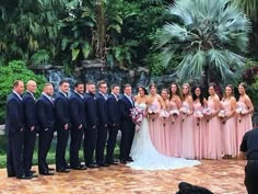 a group of people standing next to each other in front of trees and bushes at a wedding