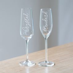 two wine glasses sitting on top of a wooden table next to each other with the word happily married written in cursive writing