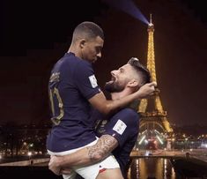 two soccer players hugging each other in front of the eiffel tower at night