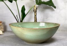 a green bowl sitting on top of a counter next to a plant